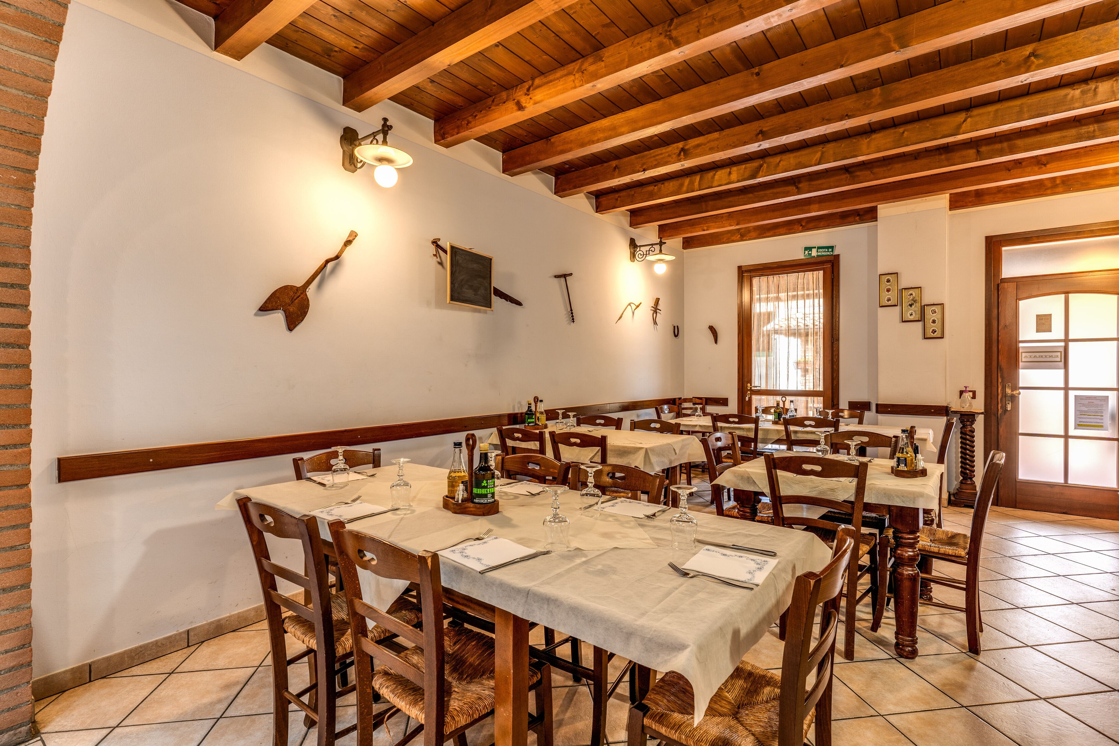 A dining area with wooden tables and chairs, white tablecloths, and wall-mounted lights.