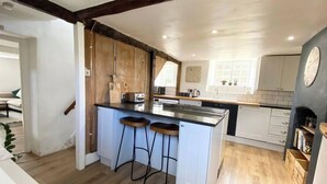 A kitchen with a central island, wooden cabinets, and a tiled backsplash. - 2 Bedroom Cottage - Sleeps 4 - Wifi, Fireplace (Sturminster Newton)