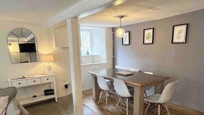 A dining area with a wooden table and white chairs, a white console table with drawers, a mirror, and framed artwork on the wall. - 2 Bedroom Cottage - Sleeps 4 - Wifi, Fireplace (Sturminster Newton)