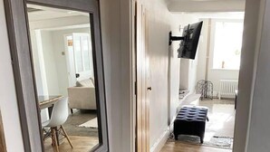 A hallway with a mirror, a television mounted on the wall, a bench, and a door leading to another room. - 2 Bedroom Cottage - Sleeps 4 - Wifi, Fireplace (Sturminster Newton)
