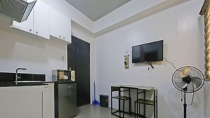 A compact kitchen with white cabinets, a microwave, a sink, a small refrigerator, a TV mounted on the wall, and a standing fan. - Bernbon Condominiuim Manila (Manila)