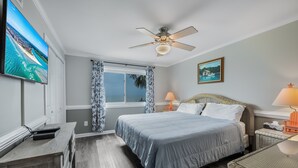A bedroom with a bed, a ceiling fan, a TV, a window with curtains, and a painting on the wall.