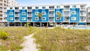 A beachfront hotel with a row of blue and white buildings, a sandy path leading to the entrance, and a clear sky. - Oceanfront 2BR • Balcony Views  & Oceanside Pool • Dog Friendly • A Summer Place B8 (North Myrtle Beach)