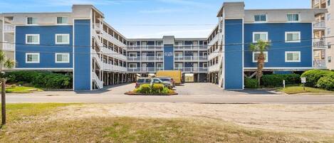 Een meerlaags hotel met een centrale binnenplaats, balkons en een parkeerplaats.