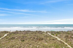 Ein Küstenpfad, der zum Strand führt, bei blauem Himmel.
