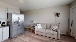 Un espacio habitable compacto con kitchenette, un sofá, una lámpara y una escoba.