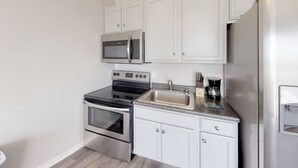 Una cocina moderna con electrodomésticos de acero inoxidable, armarios blancos, encimera de granito y una cafetera.