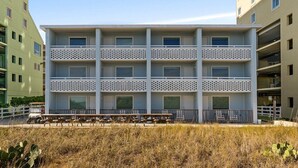 Un edificio de varios pisos con balcones, techo plano y una zona de estacionamiento con bancos.