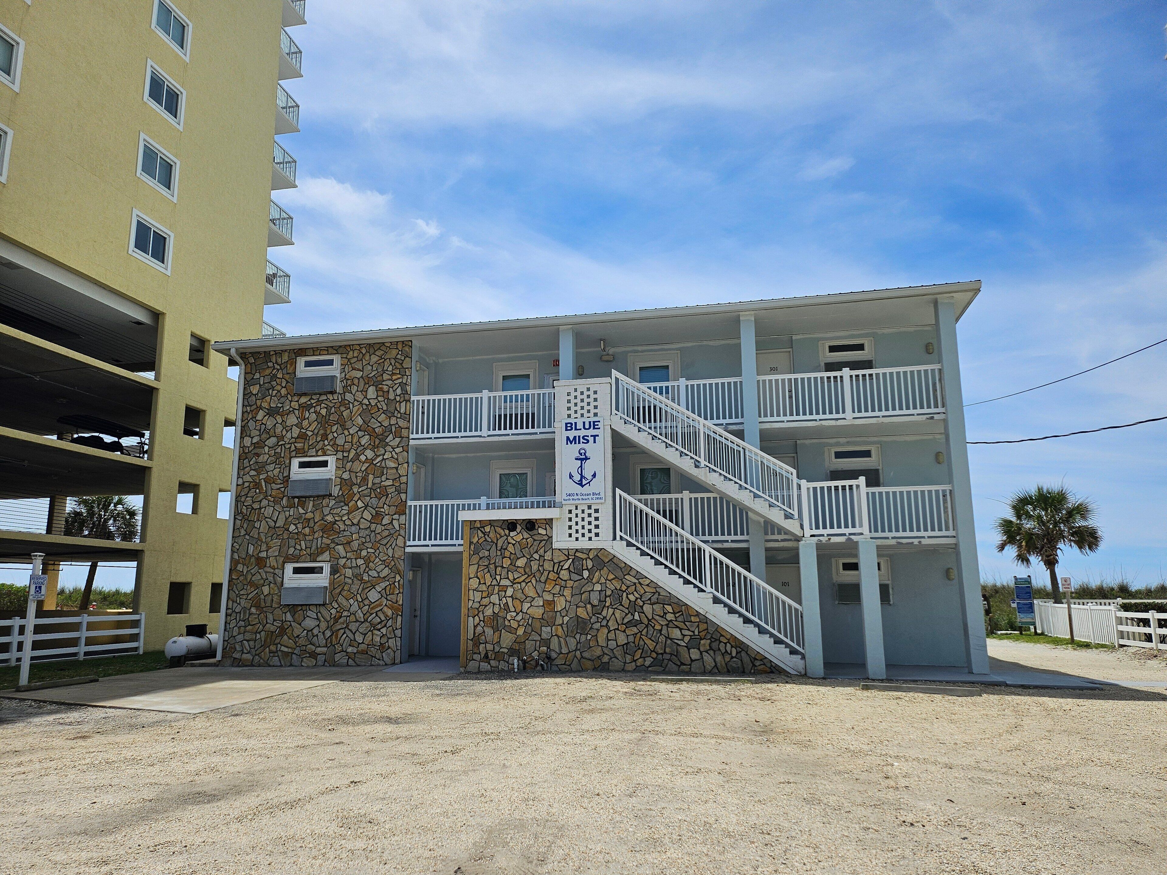 Un immeuble à plusieurs étages, doté d’une façade en pierre, d’un balcon au deuxième étage et d’une enseigne indiquant qu’il s’agit de l’hôtel « Blue Mist Inn ».