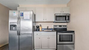 A compact kitchen with a stainless steel refrigerator, microwave, oven, and a sink with a faucet.