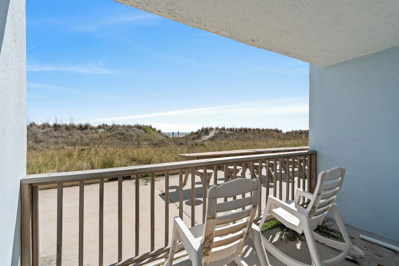 Een balkon met twee schommelstoelen met uitzicht op een strand met duinen.