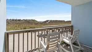 A balcony with two rocking chairs overlooking a beach with dunes.