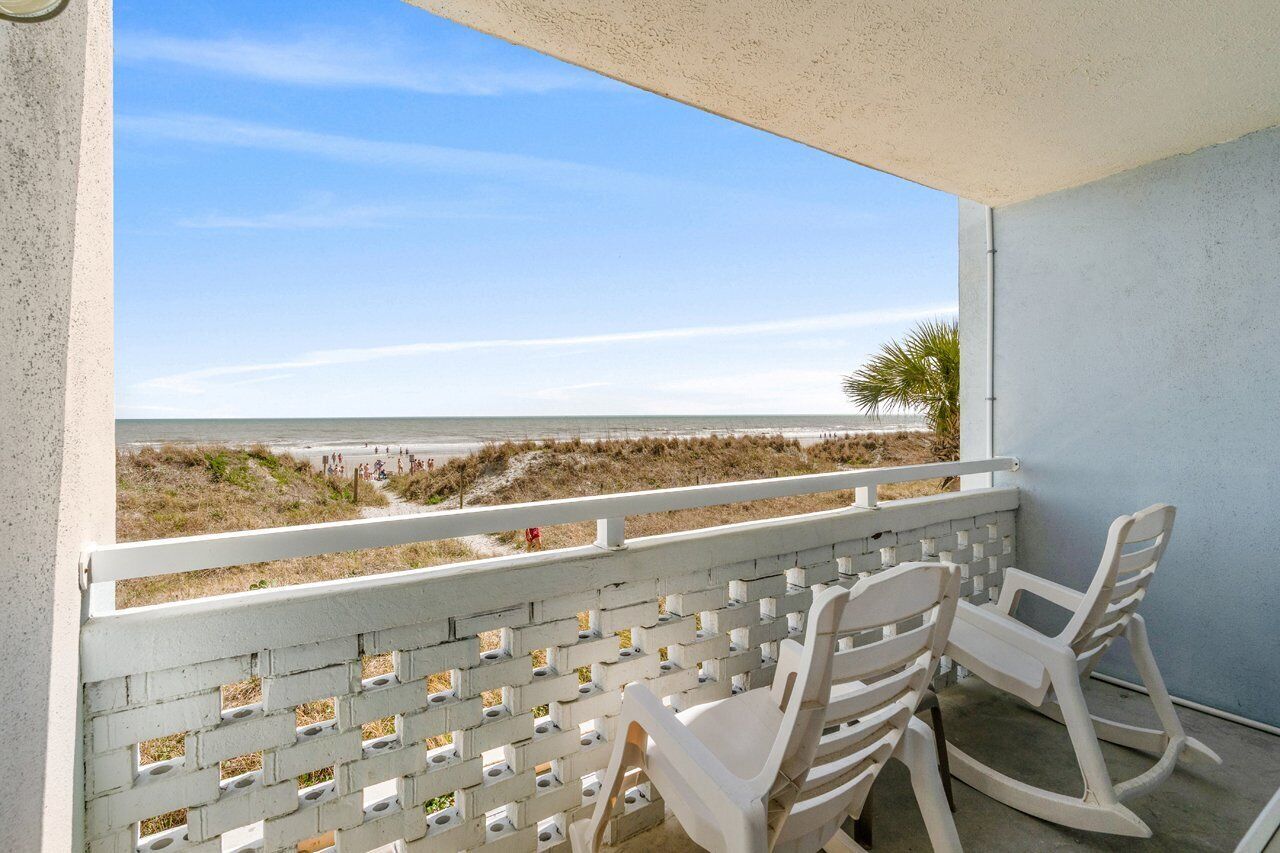 A balcony with a view of the beach, white chairs, and a white lattice railing.