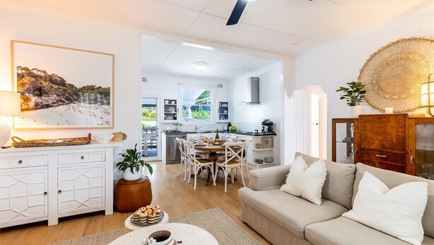 Ein modernes Wohnzimmer mit einem beigefarbenen Sofa, einem Essbereich mit einem Holztisch und einer Küche im Hintergrund.