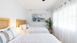 Ein Schlafzimmer mit zwei Betten, einem großen Fenster mit transparenten Vorhängen, einem Wandbild und einem Blumentopf.