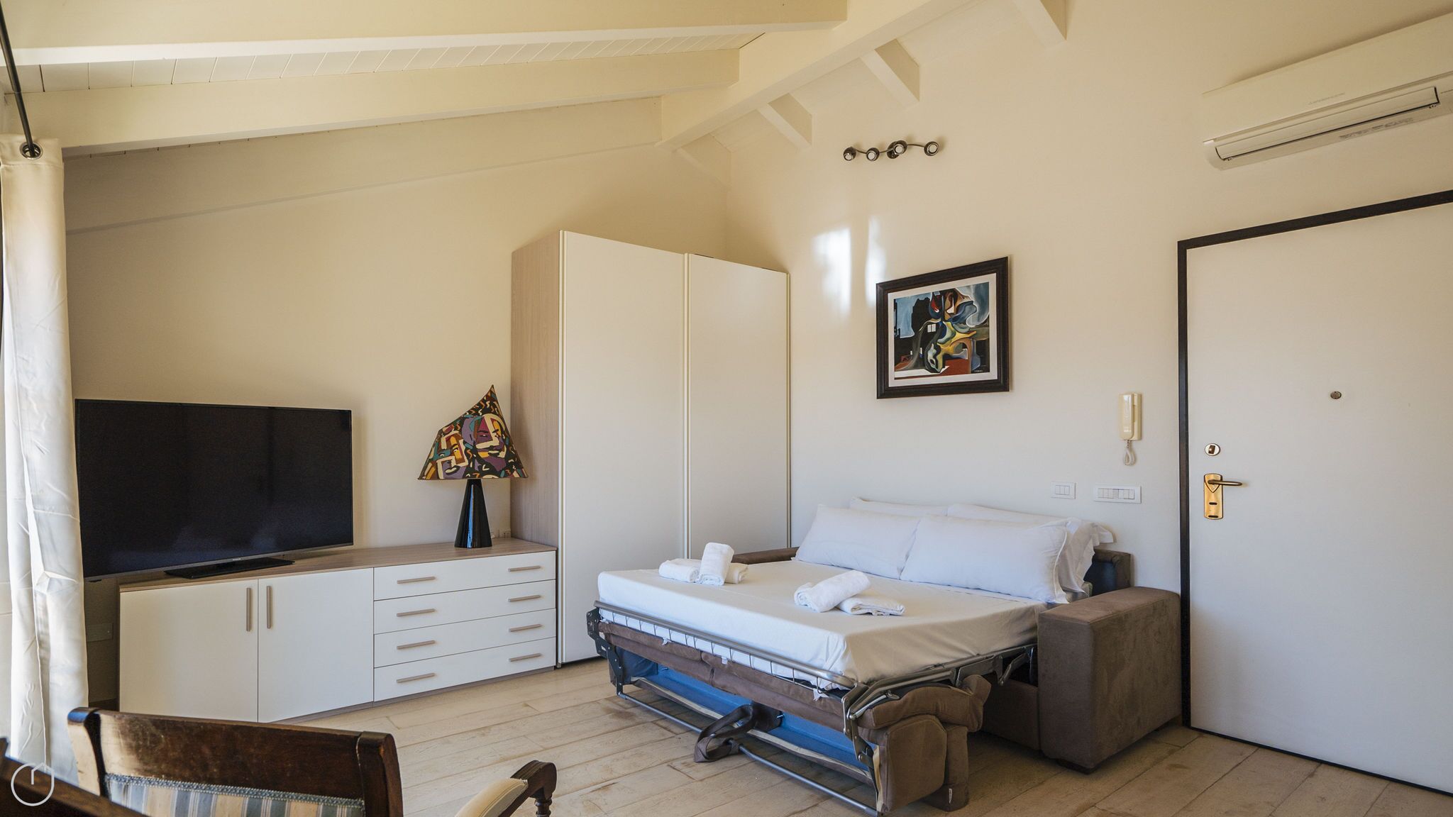 Un dormitorio con cama, televisión, armario, un cuadro y una puerta.