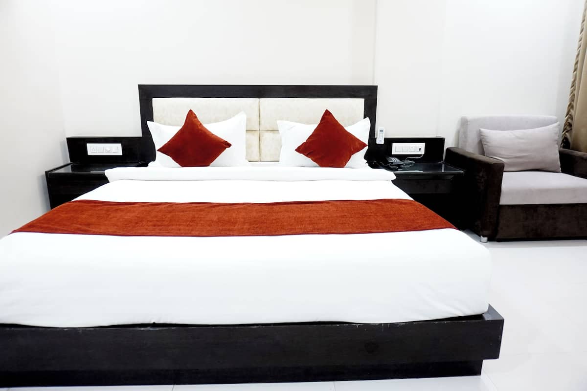 A modern hotel room with a large bed, a nightstand, a chair, and a bedside table.