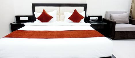 A modern hotel room with a large bed, a nightstand, a chair, and a bedside table.