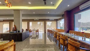 A modern hotel dining area with a central island, long dining tables, and comfortable seating. - The Aanandam Hotel Resort (Itarsi)
