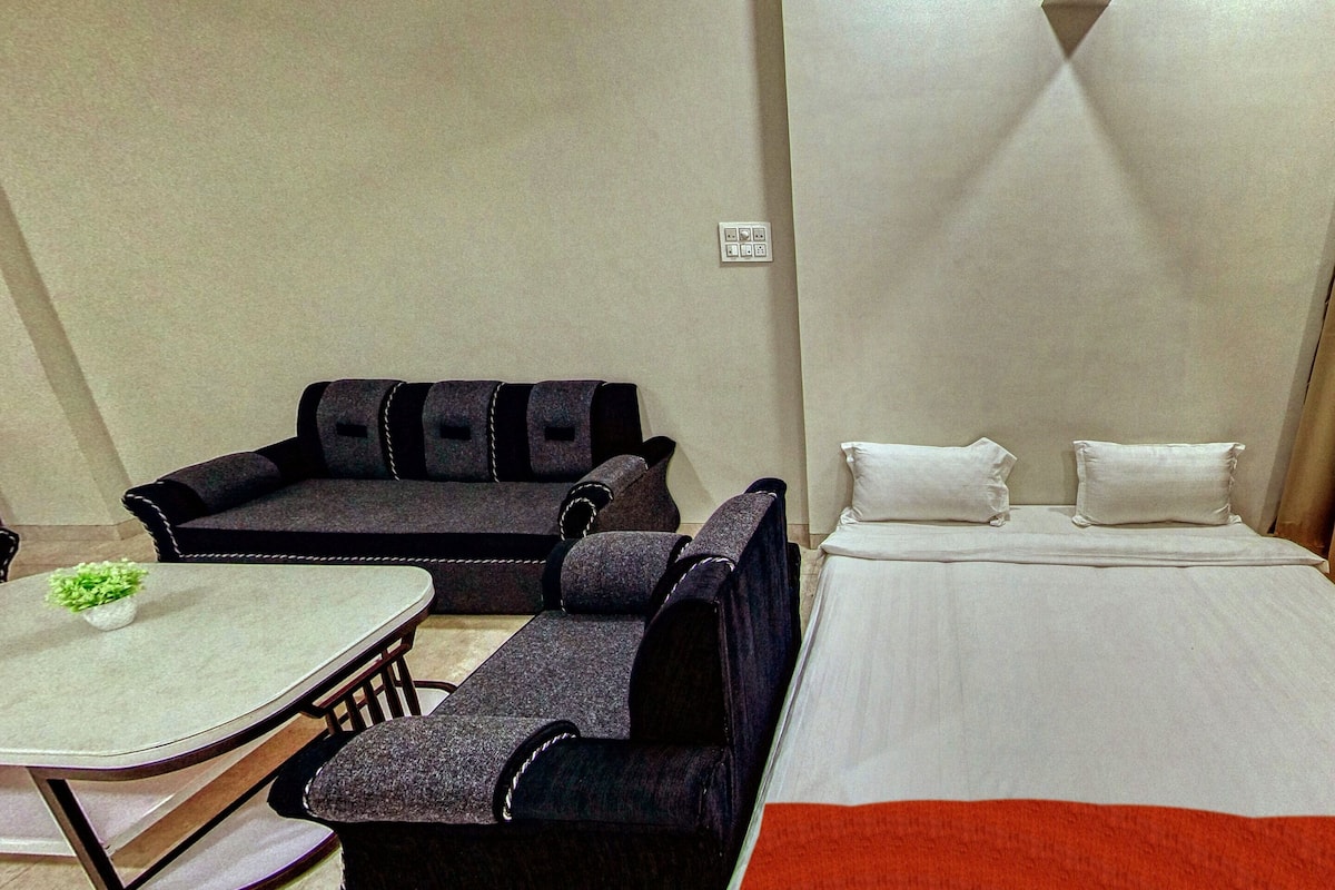 A hotel room with a bed, a sofa, a small table, and a curtain.