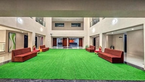 A lobby with a green carpet, red sofas, and a large window. - The Aanandam Hotel Resort (Itarsi)