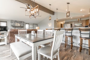 A modern kitchen with a dining area, featuring a large island, pendant lighting, and a stone fireplace.