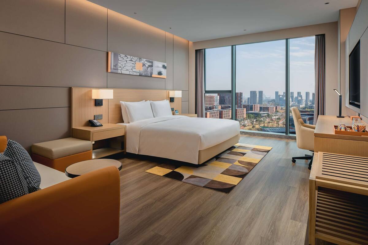 A modern hotel room with a large bed, a desk, and a view of the city.