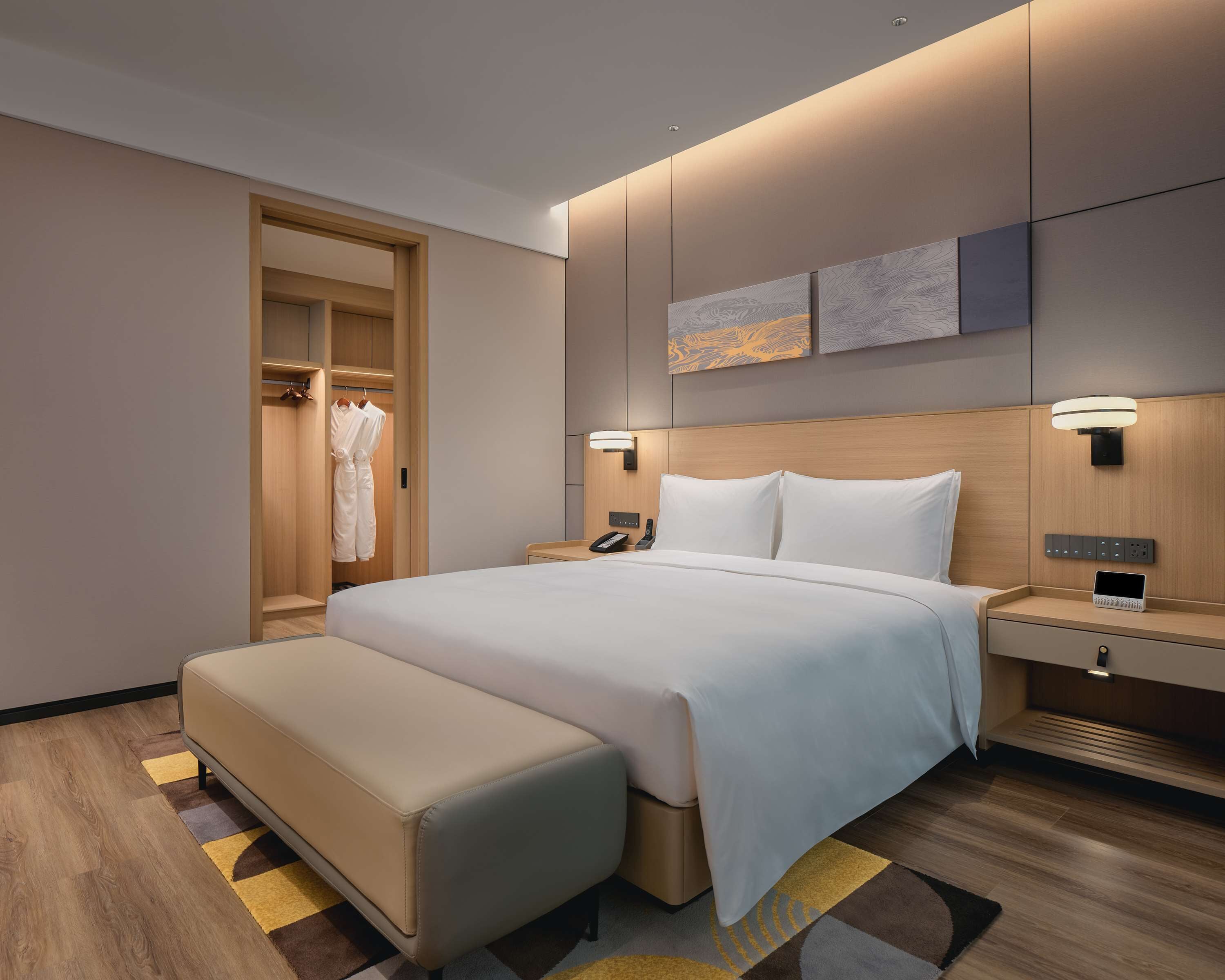 A modern hotel room with a large bed, bedside tables, a wardrobe, and a seating area.