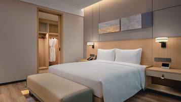 A modern hotel room with a large bed, bedside tables, a wardrobe, and a seating area.