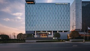 Un hôtel Hyatt Place moderne, doté d’une façade en verre, situé en milieu urbain, sous un ciel dégagé.