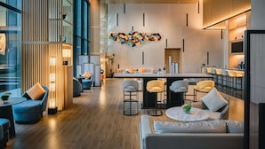 Un hall d’hôtel moderne doté d’un espace de restauration central, de différents types de sièges et d’une œuvre d’art décorative murale.