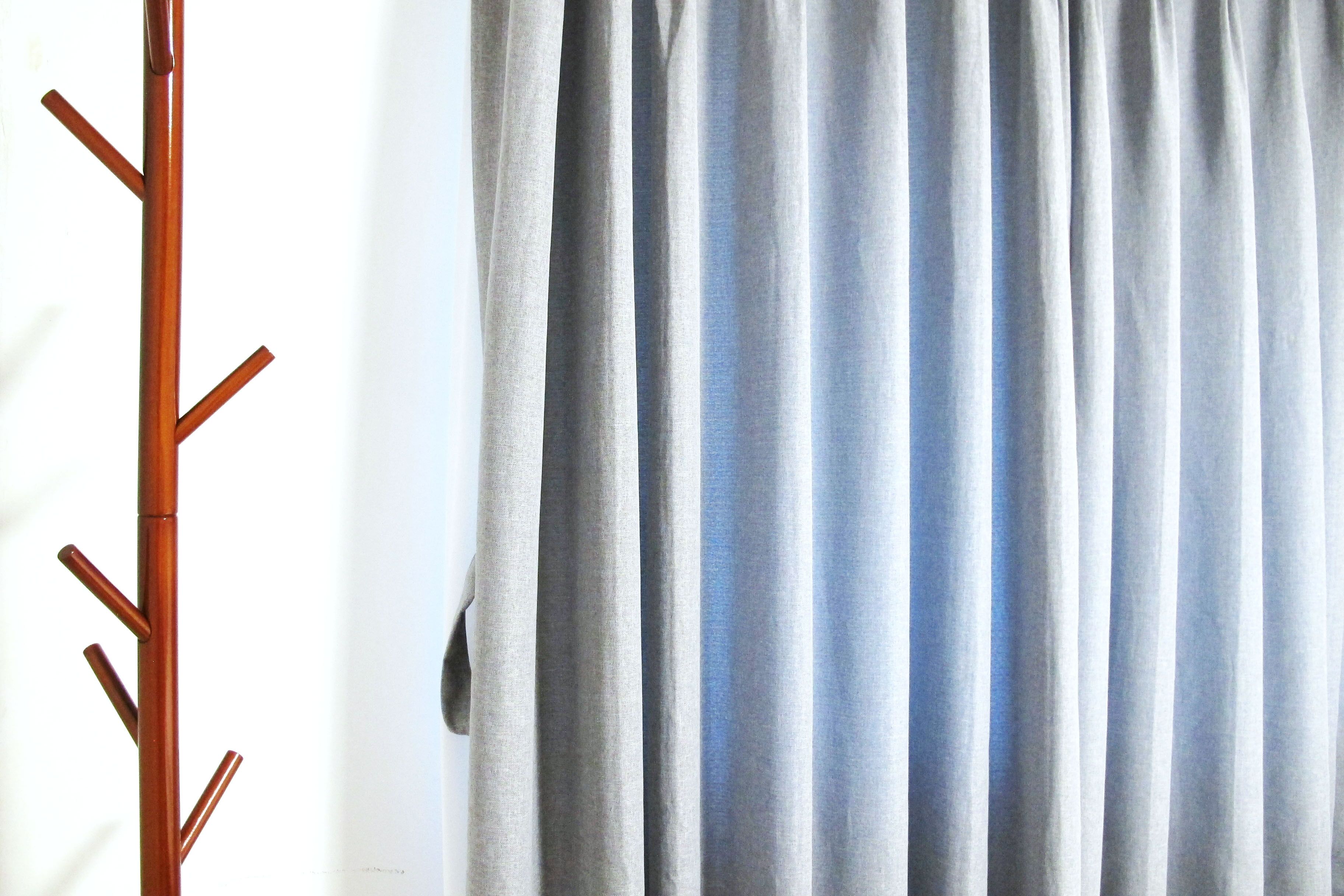 A coat rack with multiple hooks and a grey curtain in the background.