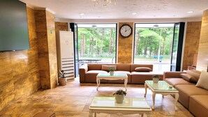 A modern lobby with a sofa, two glass-top tables, a clock, and a view of trees through large windows. - Mt Seorak the East Sea and Hot spring (Sokcho)