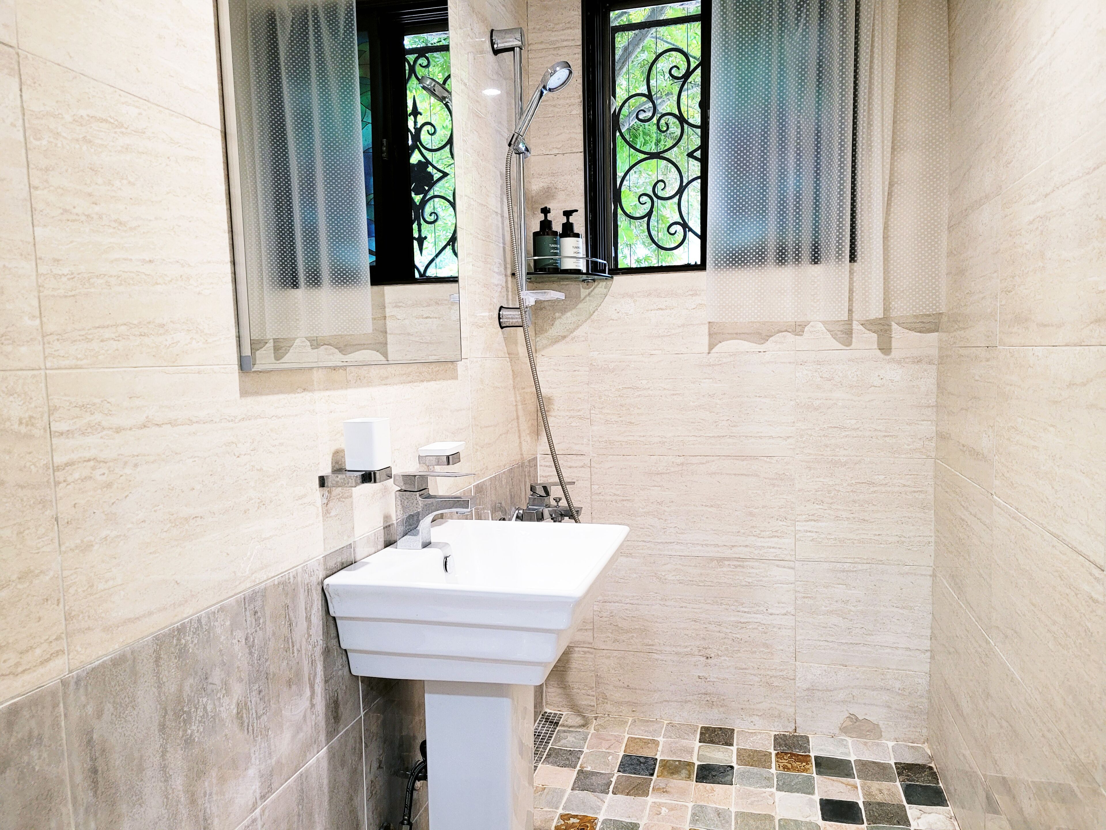 Um banheiro pequeno com pia branca, chuveiro e janela com grades de ferro decorativas.