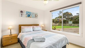 A bedroom with a large window, a bed with patterned bedding, two bedside tables with lamps, and artwork on the wall. - Views on Bayview - in Cowes (Cowes)