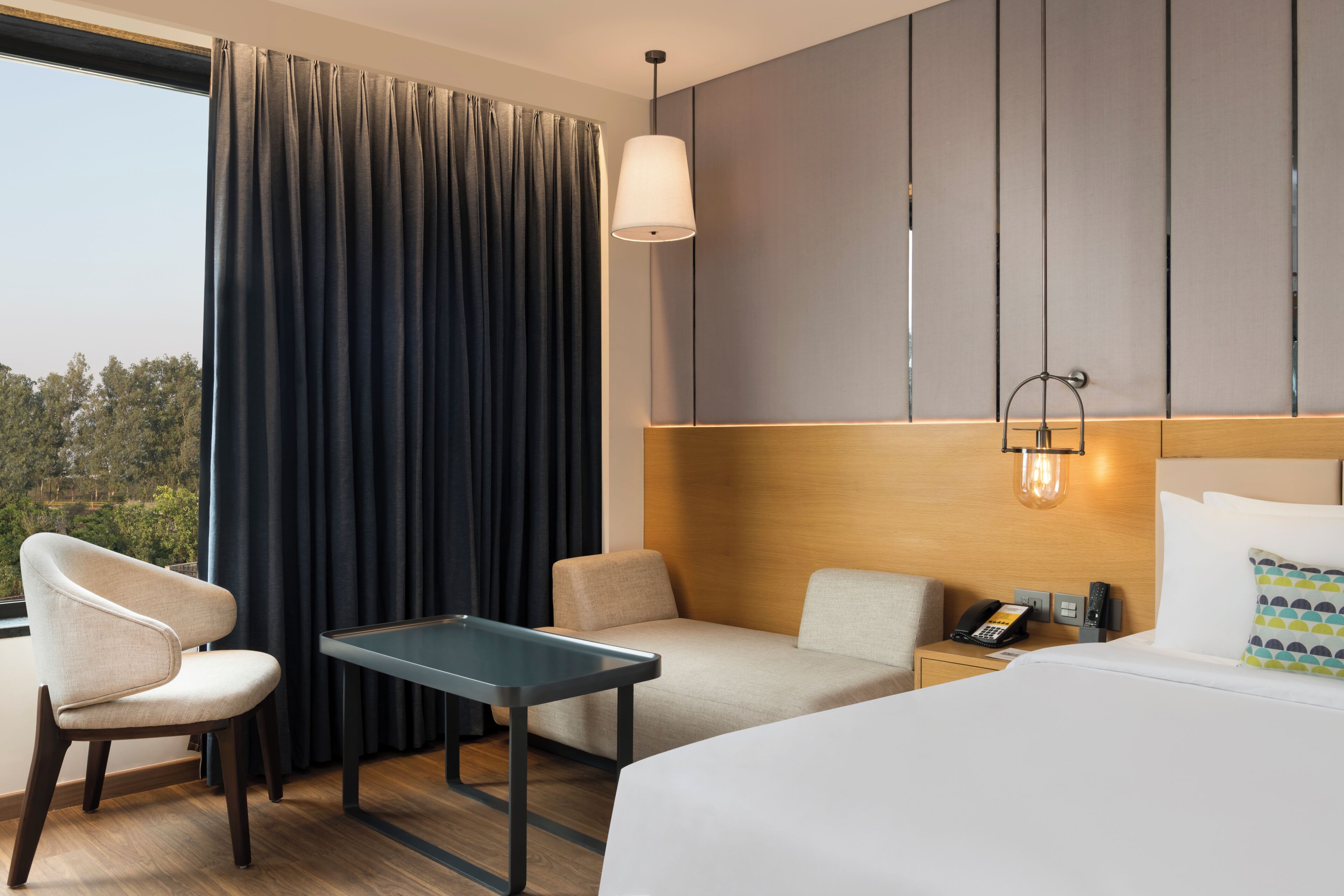 A hotel room with a bed, a desk, two chairs, a telephone, and a wall-mounted light fixture.