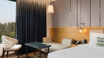 A hotel room with a bed, a desk, two chairs, a telephone, and a wall-mounted light fixture.