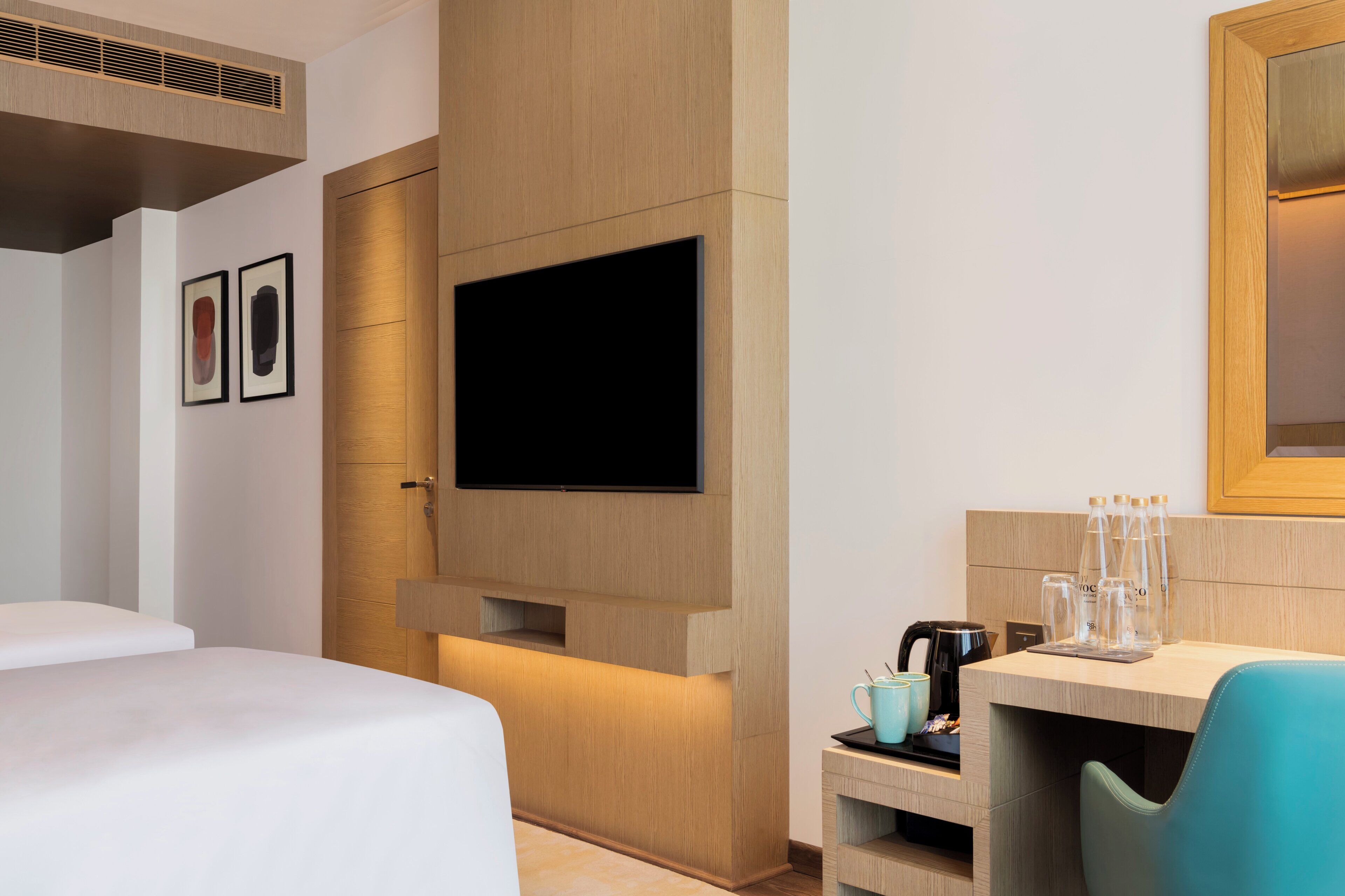 Ein modernes Hotelzimmer mit Wandfernseher, einer Holzvertäfelung, einem kleinen Tisch mit Kaffeemaschine und einem blauen Sessel.