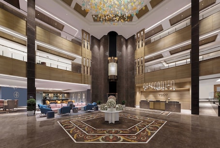 Un hall espacioso con mostrador de recepción central, zonas de estar y un candelabro decorativo.