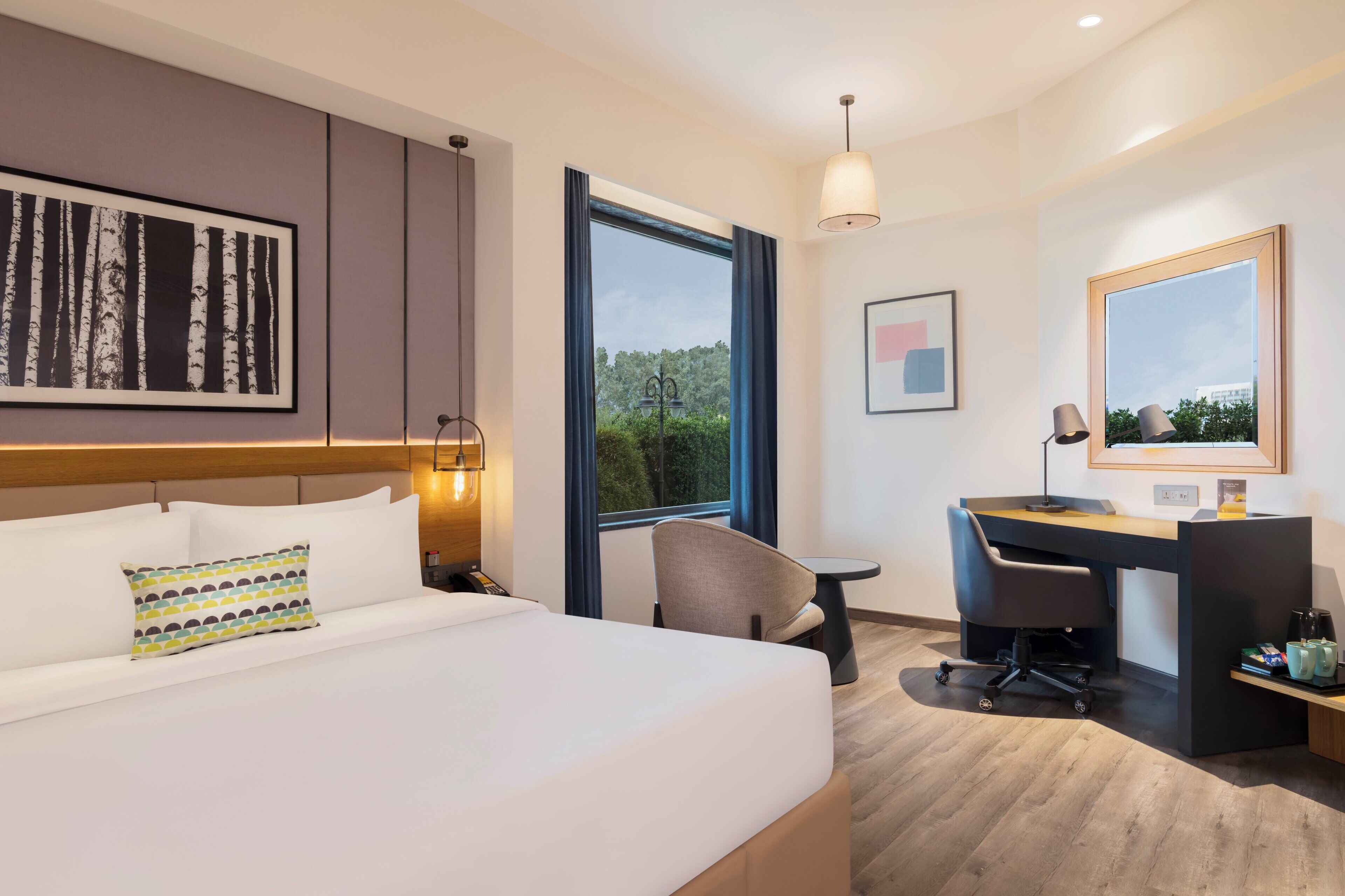 Habitación de hotel con cama, escritorio, silla y ventanas amplias.