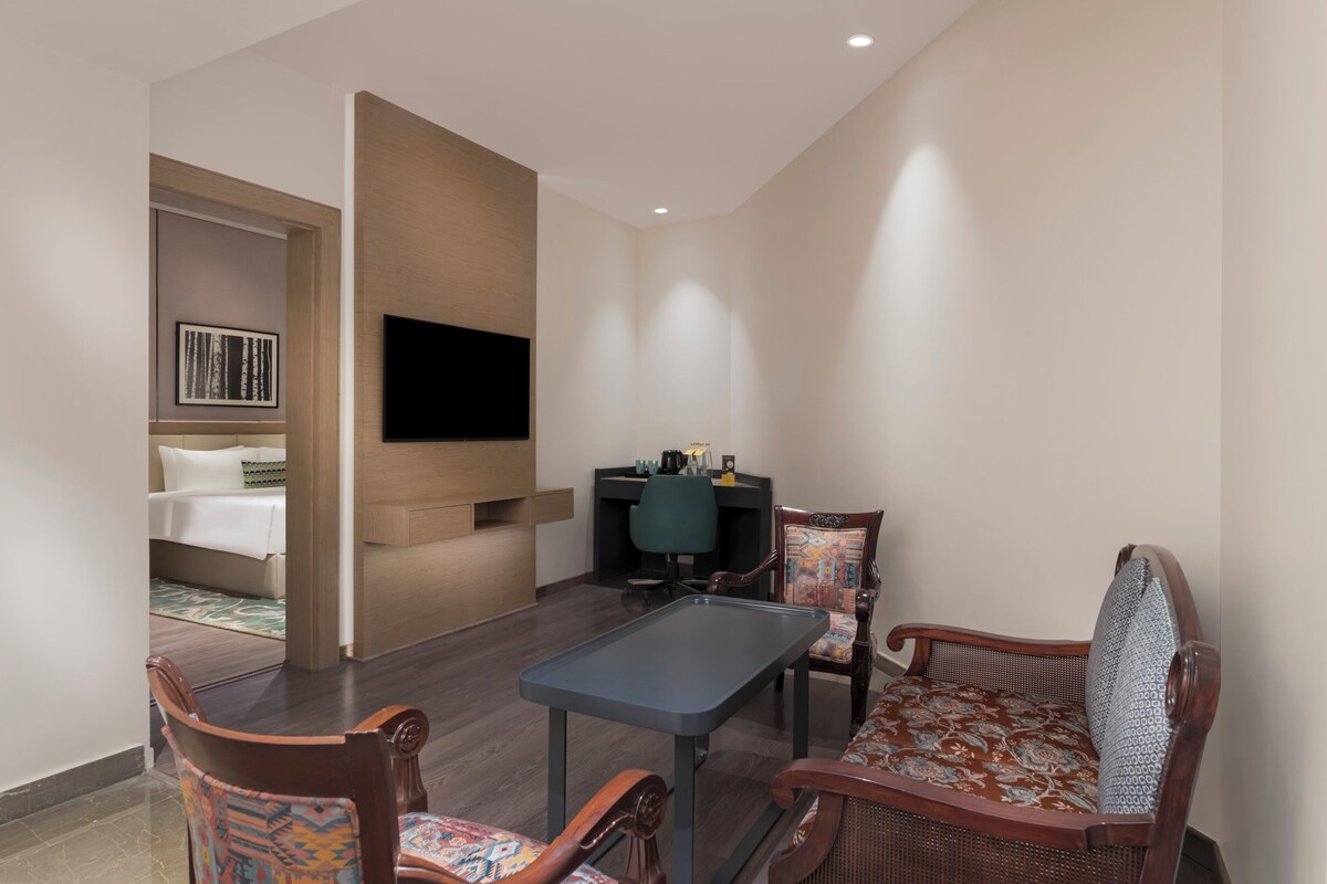 A hotel room with a bed, a desk, a TV, and two chairs.