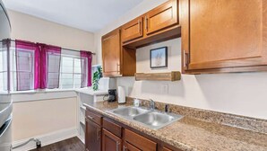 Una cocina con encimeras de granito, gabinetes de madera, un lavabo doble y una ventana con cortinas rosadas.