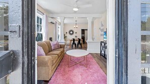 Un umbral abierto que da a un salón con un sofá color beige, una mesa redonda y una alfombra rosa.