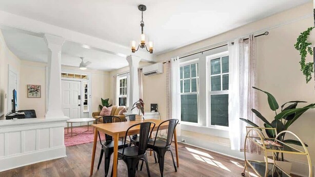 Un comedor con una mesa y sillas de madera, una araña y ventanas amplias con cortinas.