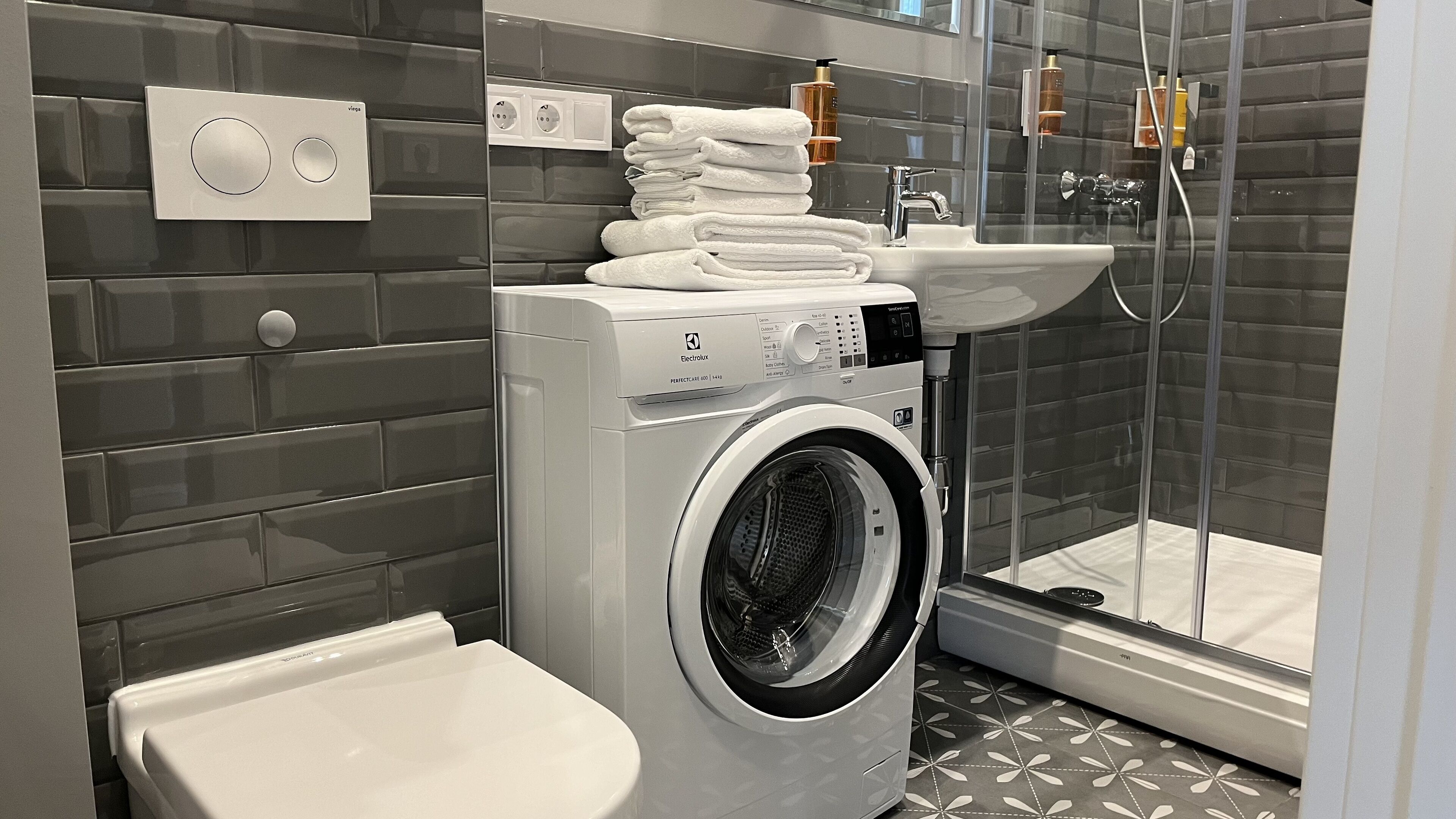 Un baño moderno con lavadora de carga frontal, lavamanos y cabina de ducha de vidrio.