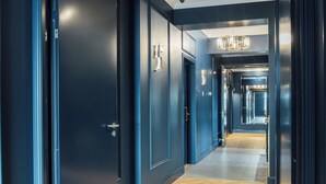 A hallway with dark blue walls, a wooden herringbone floor, and a chandelier.