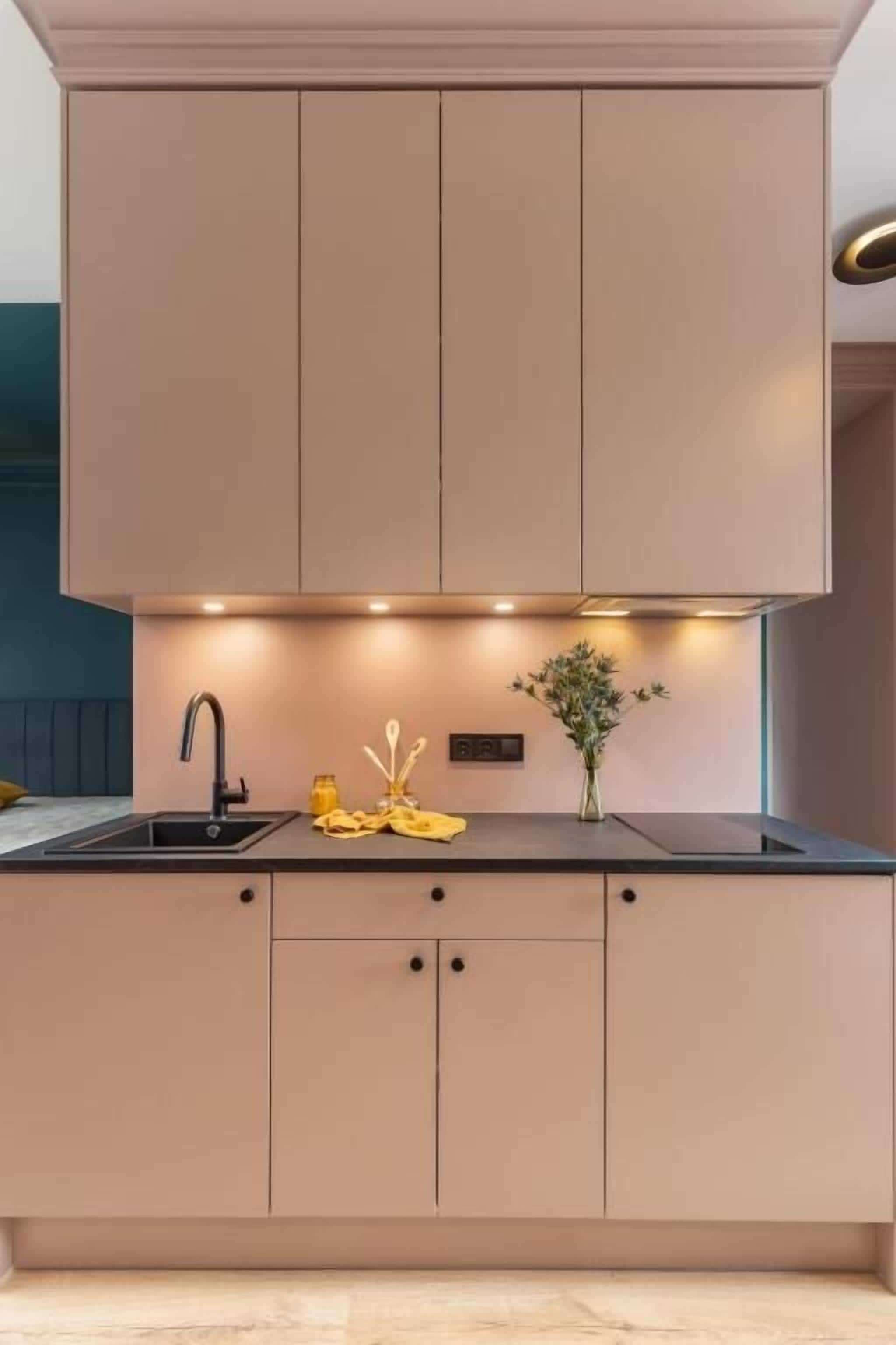 A modern kitchen with a black countertop, a sink, and cabinets. There is a vase with flowers on the countertop.