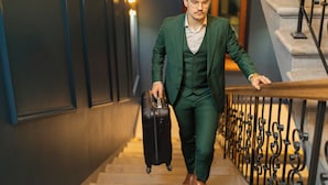 A person in a green suit walking down a staircase with a black suitcase.
