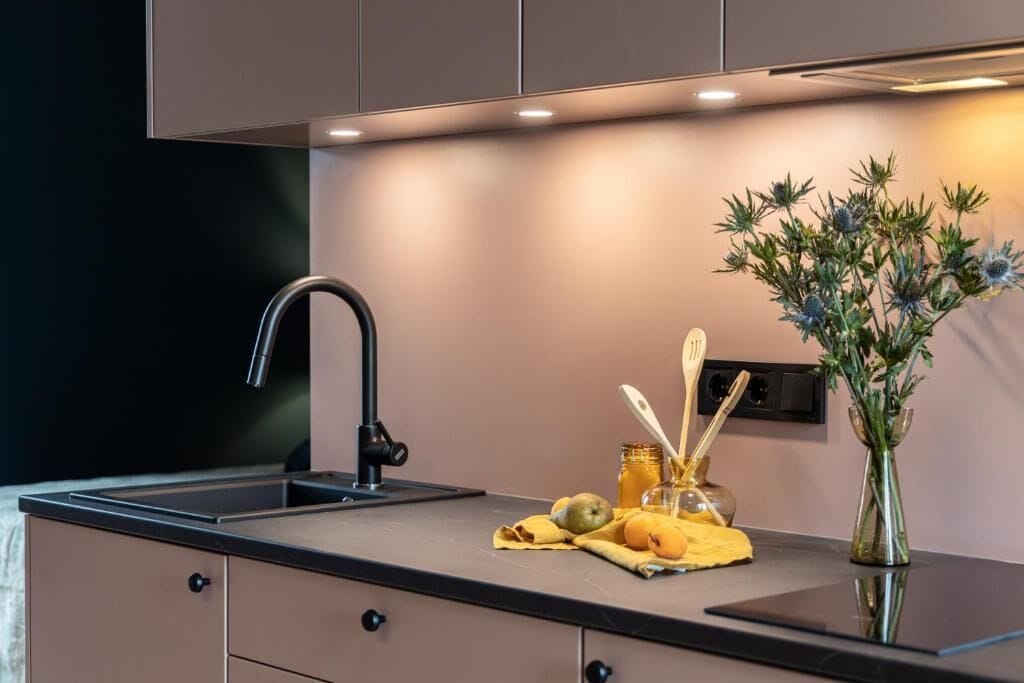 A modern kitchen with a black countertop, a stainless steel faucet, and a vase with flowers.