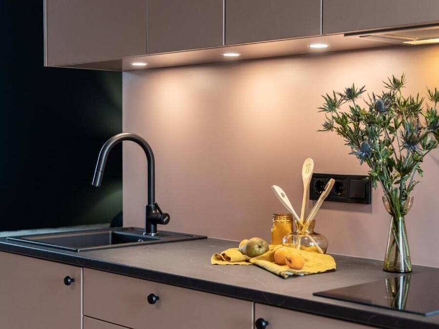 Una cocina moderna con encimera negra, grifo de acero inoxidable y un florero con flores.